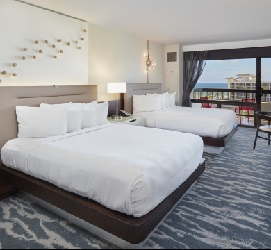 Room with two queen beds and a lit lamp in between them, window with view facing intracoastal